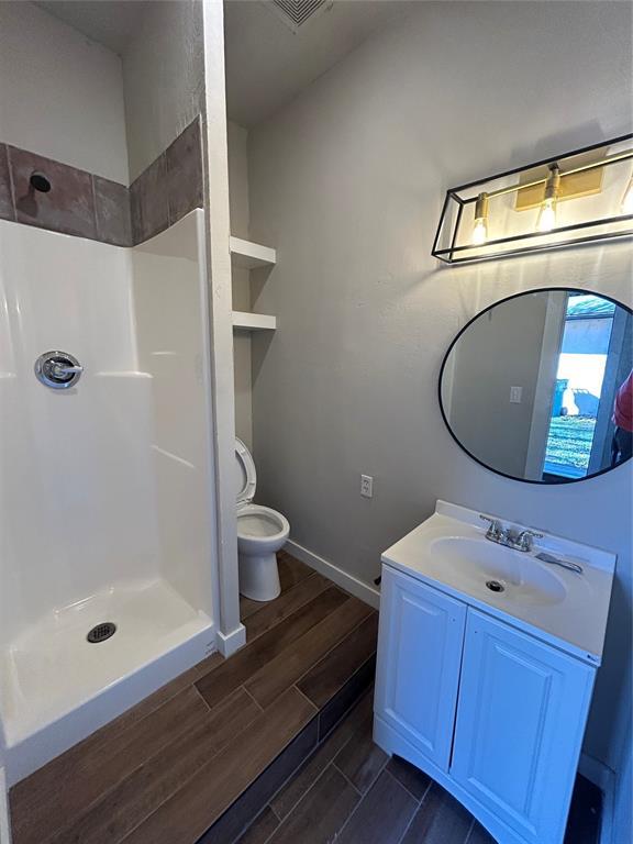 full bathroom featuring wood finish floors, toilet, a shower, baseboards, and vanity