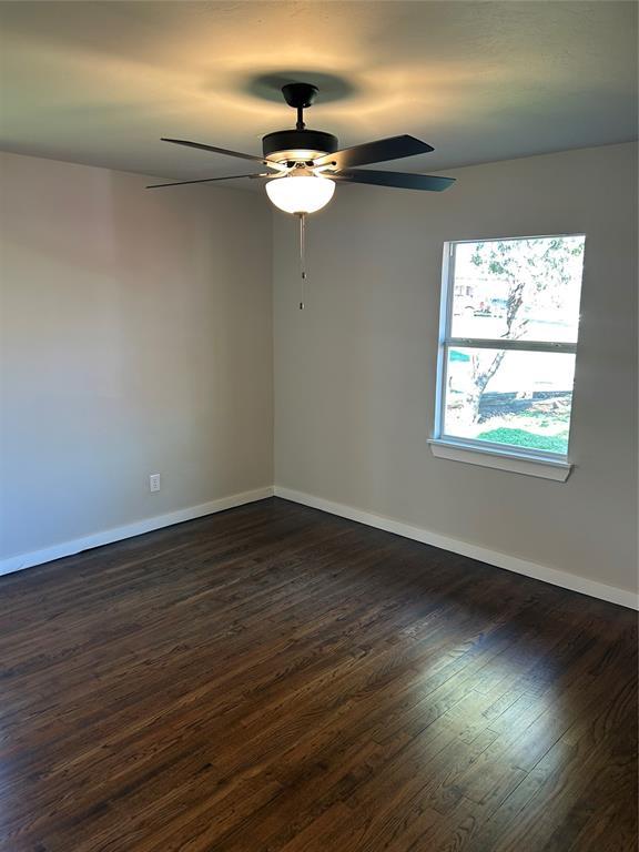 unfurnished room with dark wood-type flooring, a ceiling fan, and baseboards