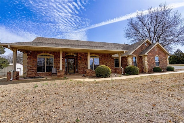 ranch-style house featuring a porch, brick siding, and a shingled roof