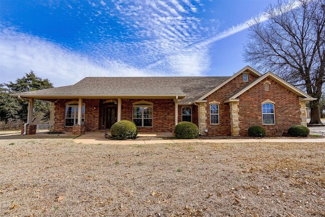 ranch-style home with brick siding, roof with shingles, and covered porch