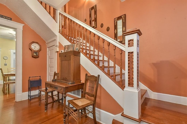 stairs with a high ceiling, decorative columns, wood finished floors, and baseboards