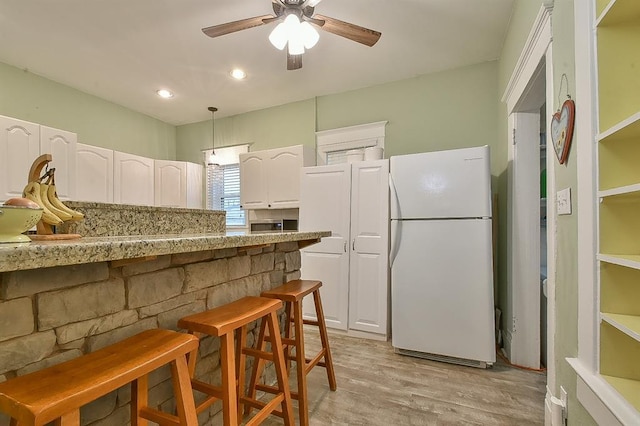 kitchen featuring a kitchen bar, light wood-type flooring, freestanding refrigerator, white cabinets, and a ceiling fan