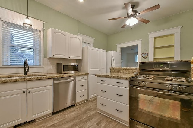 kitchen with light wood-type flooring, appliances with stainless steel finishes, white cabinets, a ceiling fan, and a sink