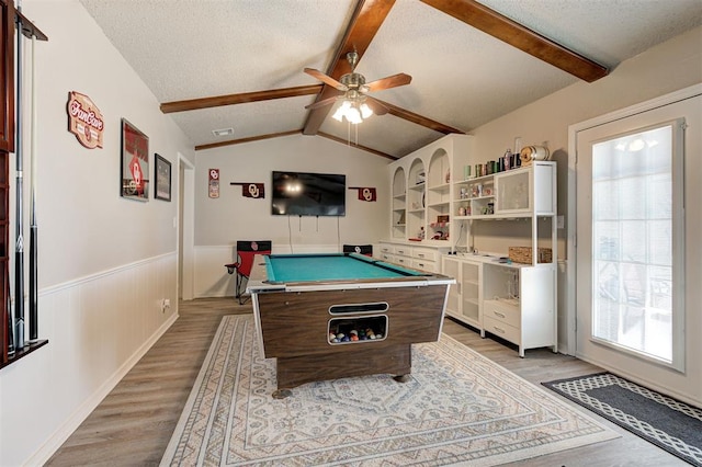 playroom with a wainscoted wall, lofted ceiling with beams, a textured ceiling, and light wood-type flooring