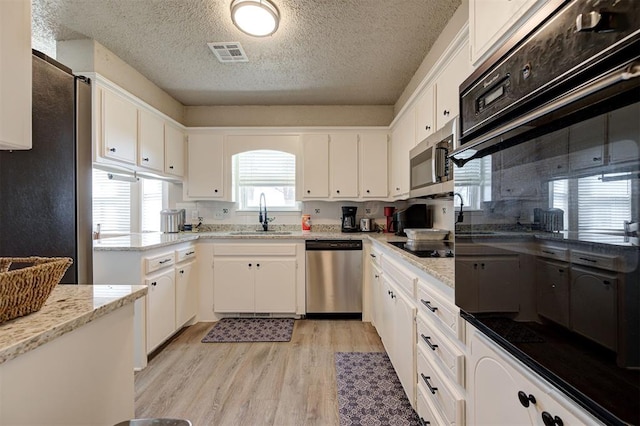kitchen featuring visible vents, light wood finished floors, a sink, stainless steel appliances, and white cabinetry