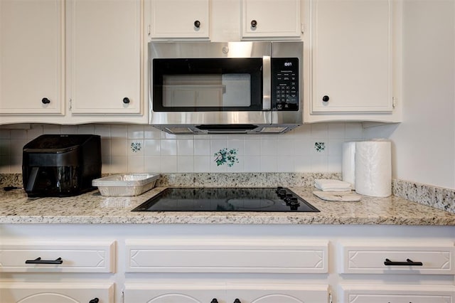 kitchen featuring stainless steel microwave, white cabinets, black electric cooktop, and backsplash