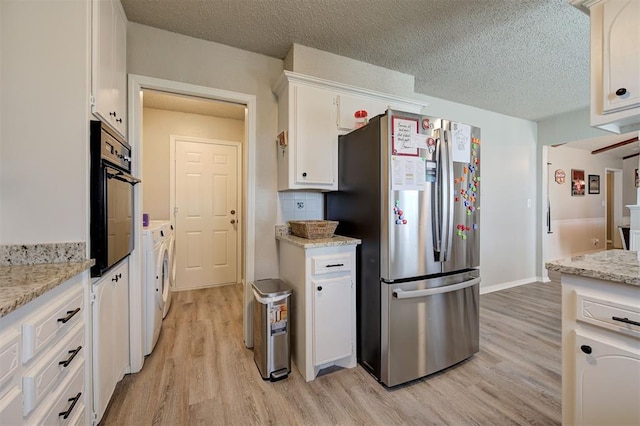 kitchen featuring washer and dryer, black oven, light wood-type flooring, and freestanding refrigerator