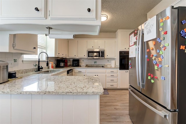 kitchen with a peninsula, light wood-style floors, a textured ceiling, black appliances, and a sink