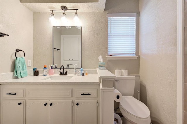 bathroom with vanity, toilet, and a textured wall
