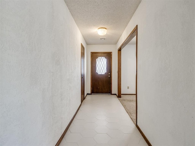 doorway to outside with visible vents, a textured ceiling, light tile patterned flooring, baseboards, and a textured wall