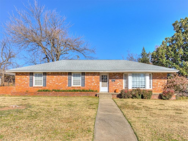 ranch-style home featuring brick siding, a front lawn, and roof with shingles