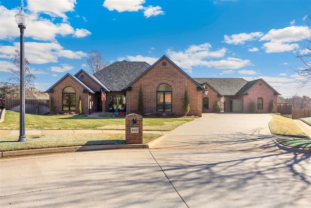 view of front of house with driveway, brick siding, a front yard, and fence