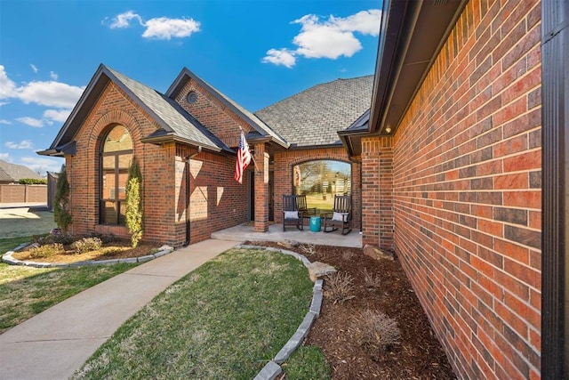 exterior space with brick siding, a patio area, a front yard, and roof with shingles