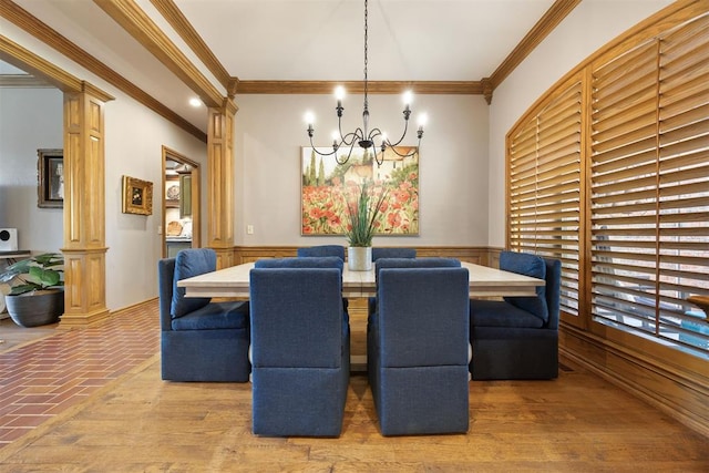 dining space with wood finished floors, an inviting chandelier, decorative columns, wainscoting, and crown molding