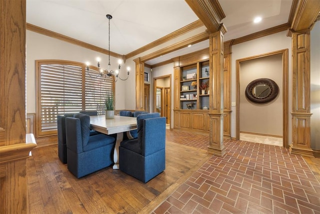 dining space with brick floor, decorative columns, a chandelier, and ornamental molding