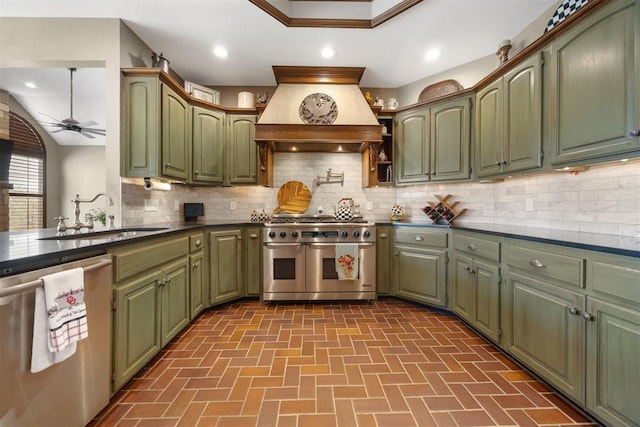 kitchen featuring dark countertops, green cabinets, custom range hood, appliances with stainless steel finishes, and a sink