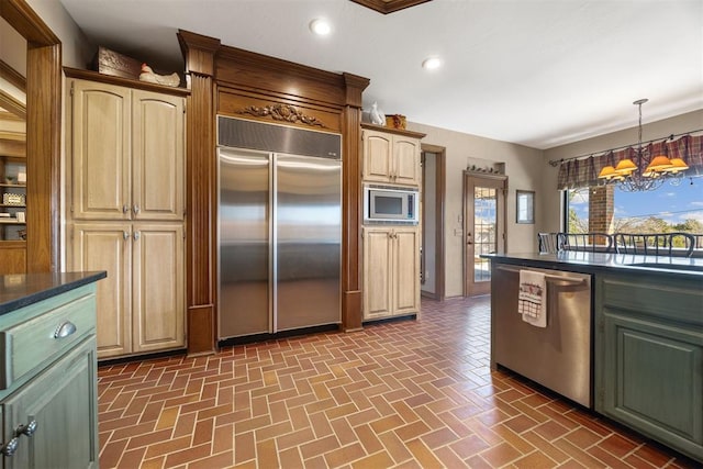 kitchen featuring dark countertops, built in appliances, recessed lighting, an inviting chandelier, and brick floor