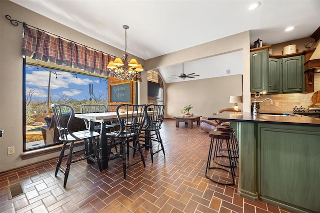 dining space with vaulted ceiling, recessed lighting, ceiling fan with notable chandelier, and brick floor