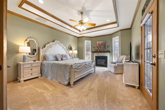 bedroom with a ceiling fan, a glass covered fireplace, carpet, crown molding, and a raised ceiling