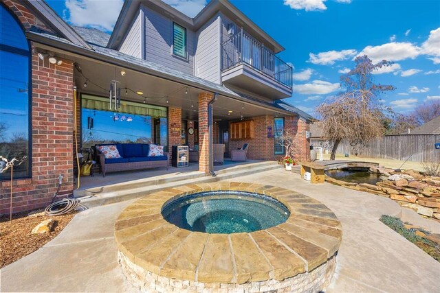 back of house with brick siding, fence, a balcony, an in ground hot tub, and a patio