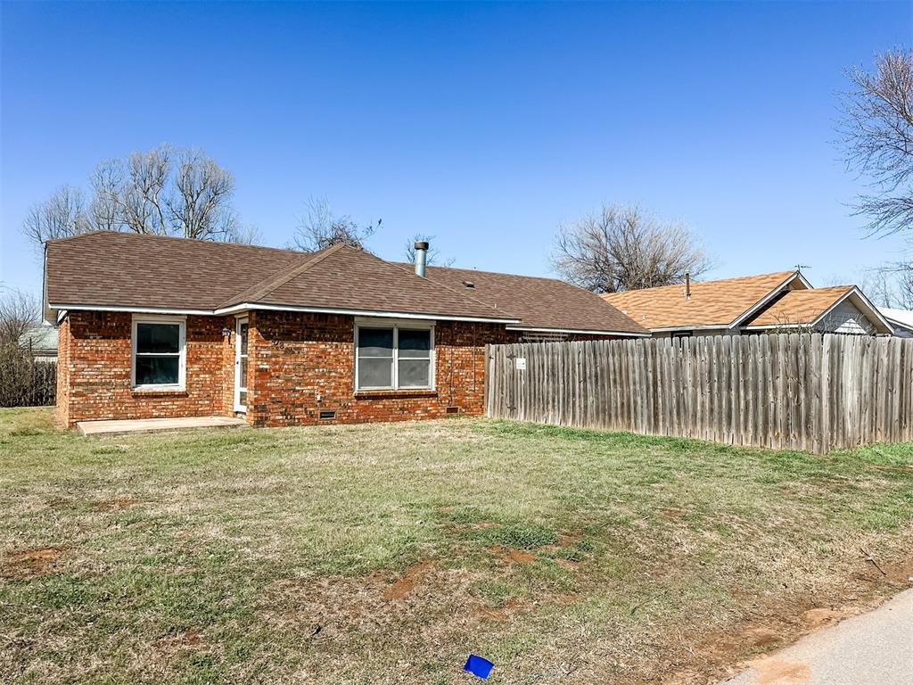 rear view of property featuring brick siding, crawl space, a yard, and fence