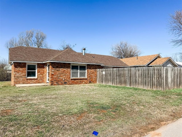 rear view of property featuring brick siding, crawl space, a yard, and fence