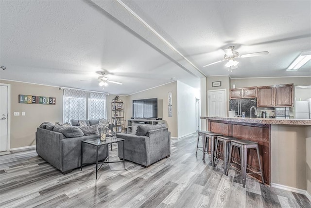 living room with light wood-style flooring, a textured ceiling, lofted ceiling, and ceiling fan