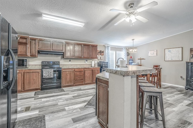 kitchen featuring under cabinet range hood, a breakfast bar area, black appliances, and light wood-style floors