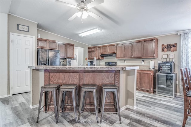 kitchen with beverage cooler, lofted ceiling, light countertops, under cabinet range hood, and black refrigerator with ice dispenser