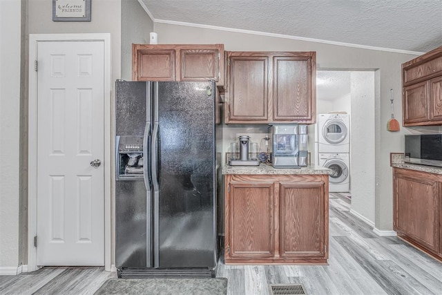 kitchen with lofted ceiling, stacked washer and dryer, a textured ceiling, stainless steel microwave, and black refrigerator with ice dispenser