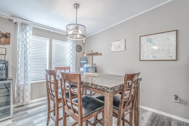 dining space with a notable chandelier, ornamental molding, a textured ceiling, wood finished floors, and baseboards