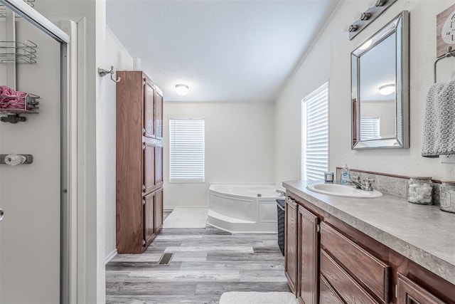 full bath with a garden tub, wood finished floors, and vanity