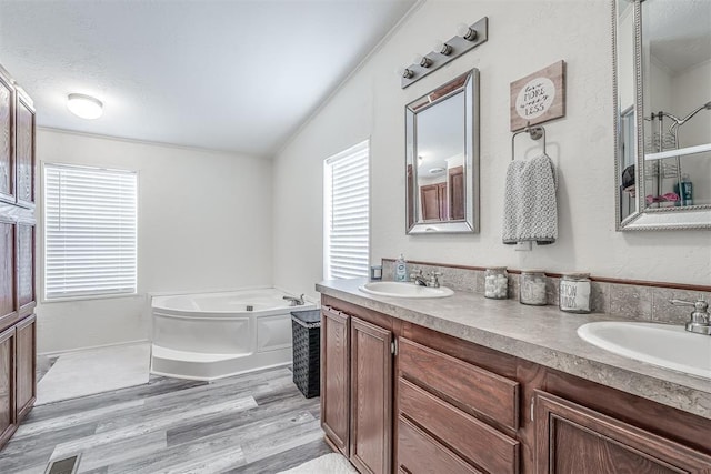 bathroom with double vanity, wood finished floors, a garden tub, and a sink