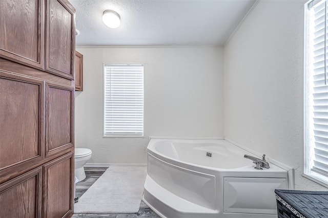 bathroom with baseboards, toilet, a textured wall, a bath, and a textured ceiling