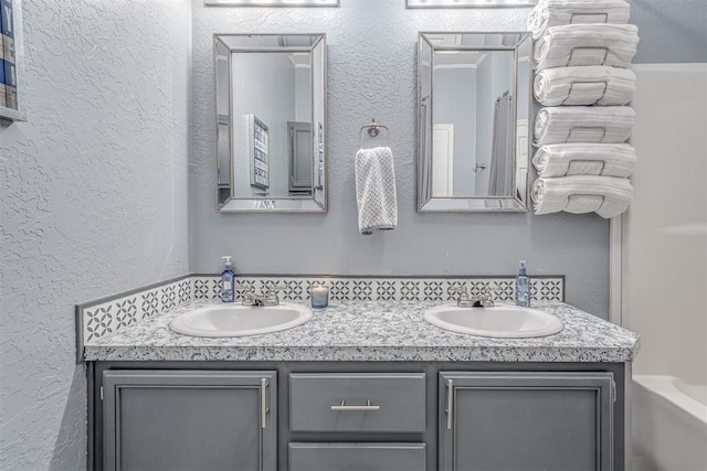 bathroom featuring double vanity, a washtub, a textured wall, and a sink