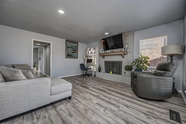 living area featuring visible vents, a brick fireplace, baseboards, wood finished floors, and a textured ceiling