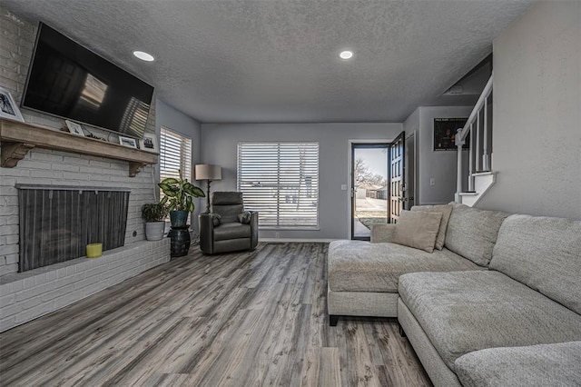 living area with a textured ceiling, wood finished floors, recessed lighting, a brick fireplace, and stairs