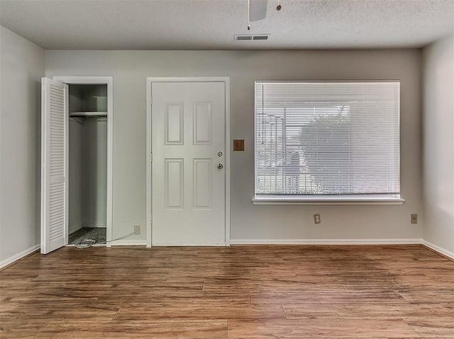 foyer entrance featuring visible vents, a textured ceiling, baseboards, and wood finished floors