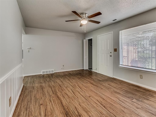 empty room with visible vents, a textured ceiling, a ceiling fan, and wood finished floors