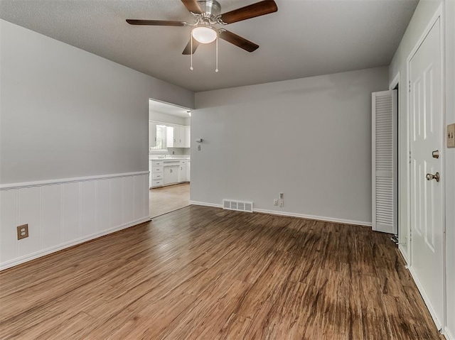 empty room featuring visible vents, a ceiling fan, wood finished floors, wainscoting, and baseboards