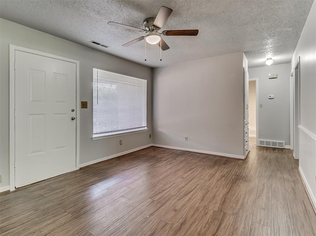 interior space with a ceiling fan, wood finished floors, visible vents, and a textured ceiling