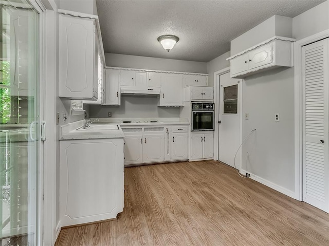 kitchen with a sink, black oven, white cabinets, light wood finished floors, and light countertops