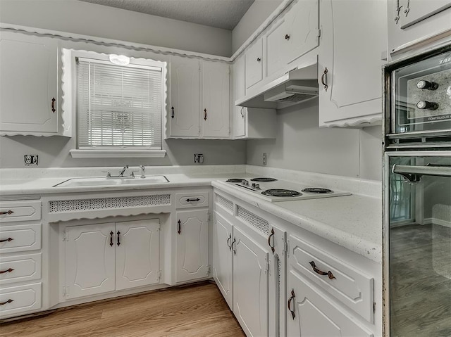 kitchen featuring light wood-style flooring, under cabinet range hood, a sink, white cabinets, and light countertops