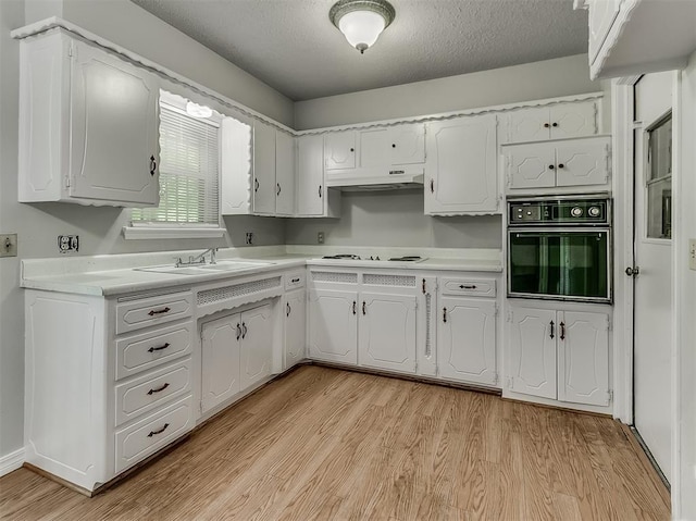 kitchen featuring black oven, light wood finished floors, white cabinets, and a sink