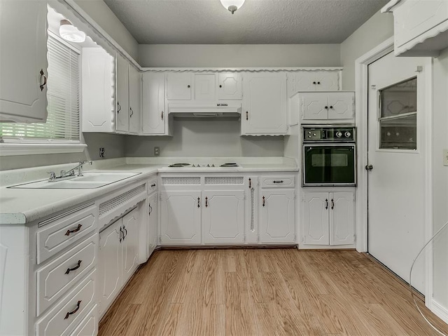 kitchen featuring black oven, light wood-type flooring, under cabinet range hood, and a sink