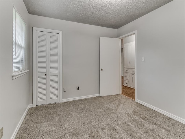 unfurnished bedroom with a closet, a textured ceiling, baseboards, and carpet floors