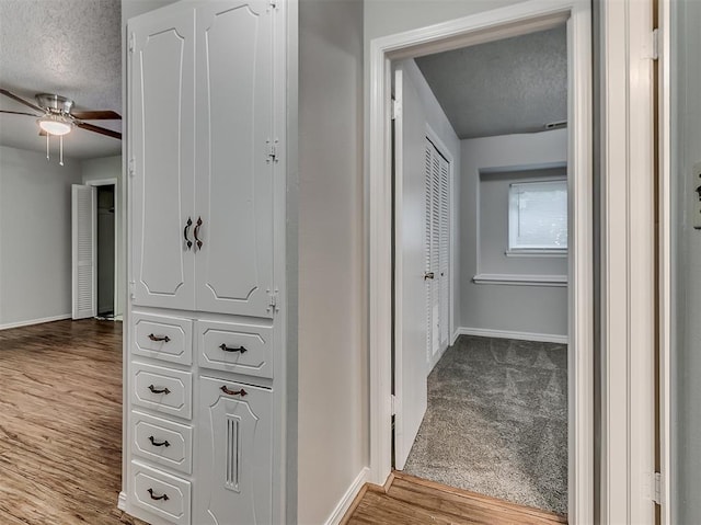 hall with baseboards, a textured ceiling, and wood finished floors