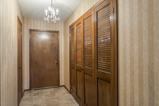 doorway to outside with a textured ceiling, baseboards, wallpapered walls, an inviting chandelier, and stone finish flooring