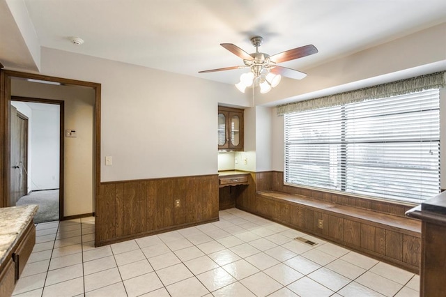 interior space with visible vents, ceiling fan, light tile patterned floors, wainscoting, and built in study area