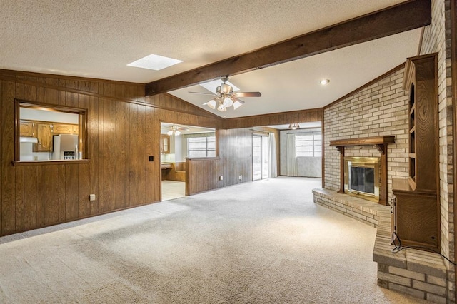 unfurnished living room with carpet floors, lofted ceiling with beams, wood walls, a textured ceiling, and a brick fireplace